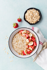 Bowl of oatmeal porridge with strawberry and banana on blue table top view. Healthy and diet breakfast.