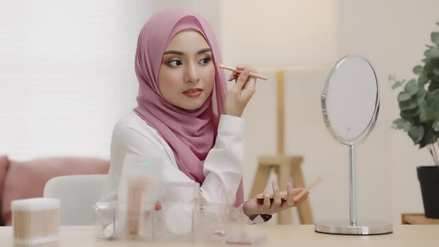 Daily routine make up young Asian beautiful muslim woman with hijab looking mirror applying eyes shadow daily routine at home. Beautiful of girl holding brush make-up on eyes.