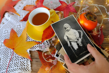 Autumn composition on rustic wooden table in garden with vintage photos, hot tea in mug, fallen...