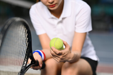 Pensive young female tennis player holding ball racket sitting on the bench at tennis court