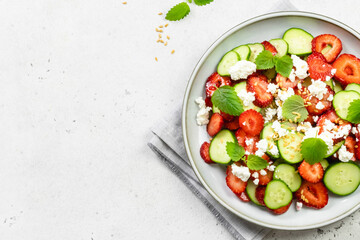 Healthy cucumber strawberry feta cheese salad with honey lemon dressing on plate. Top view, flat...