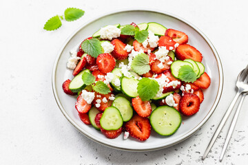 Healthy cucumber strawberry feta cheese salad with lemon dressing on plate. Top view, flat lay, copy space.