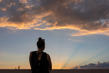 Fototapeta premium Rear view of silhouette of woman that gazes at the colorful horizon as the sun sets in Las Vegas, Nevada, USA. Clouds turn red and orange during the golden hour. Romantic atmosphere. Serenity