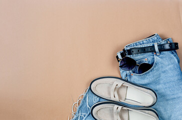 Blue jeans, beige suede loafer or flat shoes lying and sunglasses on beige background.