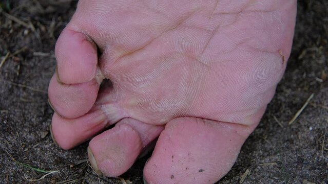 Extreme close up of slightly dirty bare foot sole with some soil in the nails while resting legs on the ground.