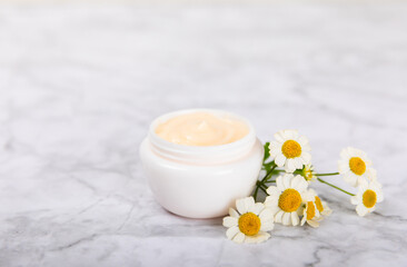 Fototapeta na wymiar Cream for body and hands with a chamomile flower on a light marble background. Herbal dermatological cosmetic hygiene cream. Natural cosmetic product. Cosmetic tube. Ecological cosmetics.Copy space.