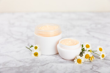 Cream for body and hands with a chamomile flower on a light marble background. Herbal dermatological cosmetic hygiene cream. Natural cosmetic product. Cosmetic tube. Ecological cosmetics.Copy space.