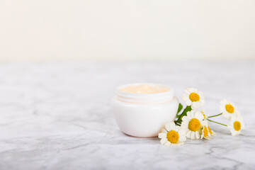 Cream for body and hands with a chamomile flower on a light marble background. Herbal dermatological cosmetic hygiene cream. Natural cosmetic product. Cosmetic tube. Ecological cosmetics.Copy space.