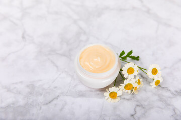 Obraz na płótnie Canvas Cream for body and hands with a chamomile flower on a light marble background. Herbal dermatological cosmetic hygiene cream. Natural cosmetic product. Cosmetic tube. Ecological cosmetics.Copy space.