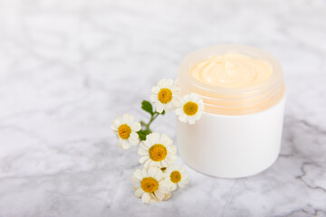 Cream for body and hands with a chamomile flower on a light marble background. Herbal dermatological cosmetic hygiene cream. Natural cosmetic product. Cosmetic tube. Ecological cosmetics.Copy space.