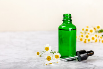 Chamomile essential oil.Glass bottle with chamomile essential oil on a marble background. Chamomile flowers, close up. Aromatherapy, spa and herbal medicine ingredients. Space for copy. Beauty concept