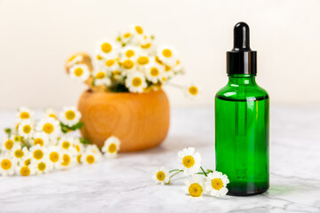 Chamomile essential oil.Glass bottle with chamomile essential oil on a marble background. Chamomile flowers, close up. Aromatherapy, spa and herbal medicine ingredients. Space for copy. Beauty concept