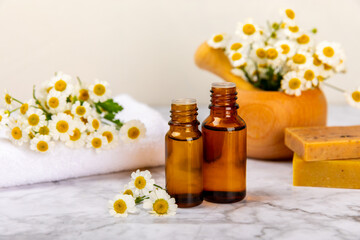 Chamomile essential oil.Glass bottle with chamomile essential oil on a marble background. Chamomile flowers, close up. Aromatherapy, spa and herbal medicine ingredients. Space for copy. Beauty concept
