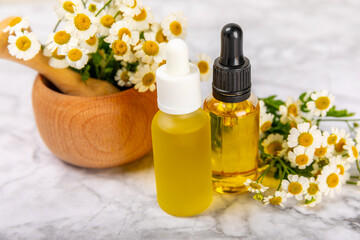 Fototapeta na wymiar Chamomile essential oil.Glass bottle with chamomile essential oil on a marble background. Chamomile flowers, close up. Aromatherapy, spa and herbal medicine ingredients. Space for copy. Beauty concept