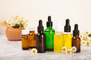 Chamomile essential oil.Glass bottle with chamomile essential oil on a marble background. Chamomile flowers, close up. Aromatherapy, spa and herbal medicine ingredients. Space for copy. Beauty concept