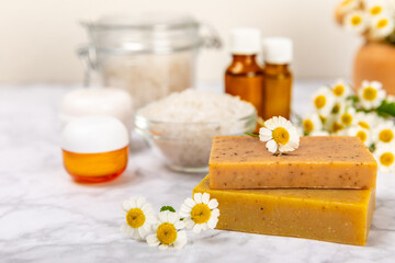 Fototapeta na wymiar Chamomile Spa. Essential oil, sea salt, chamomile flowers, body cream and handmade soap. Natural herbal cosmetics with chamomile flowers on a textured background.Beauty concept. Cosmetic tube. 