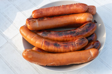 Grilled sausages are being prepared outdoors on a warm sunny day, picnic