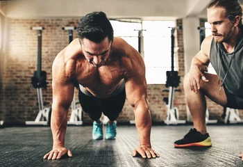 Push up, strong and man or personal trainer in gym support, motivation and helping body builder in training. Muscle, fitness and focus of people exercise or workout on floor, advice or accountability © Nikish Hiraman/peopleimages.com