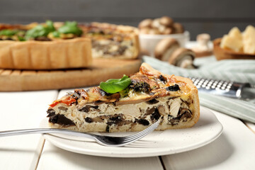 Piece of delicious quiche with mushrooms and basil served on white wooden table