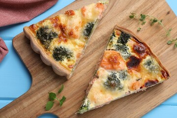 Pieces of delicious homemade quiche with salmon and broccoli on wooden board, top view