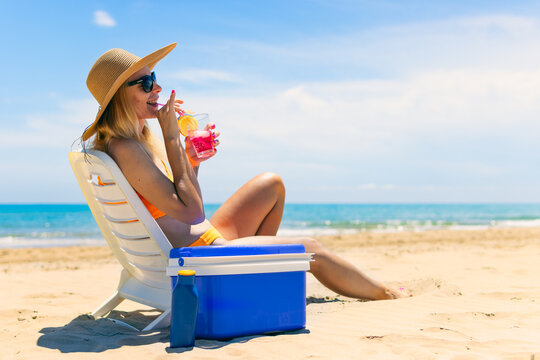 girl in a bathing suit, a hat sits on a sun lounger with a cocktail side view on the beach