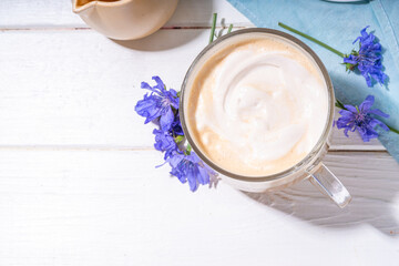  Chicory herbal coffee latte, cappuccino drink, with whipped non-dairy milk and blue flowers on white wooden table. Alternative vegan and keto diet coffee with chicory flowers and root powder