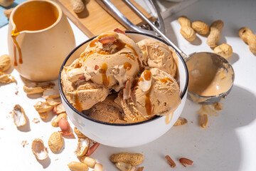Peanut butter ice cream balls. A lot nuts gelato scoops in ceramic bowl, with caramel sauce, white kitchen background copy space