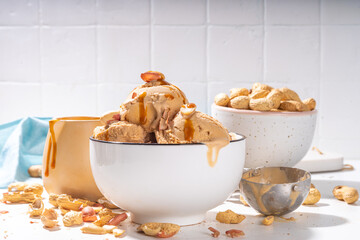 Peanut butter ice cream balls. A lot nuts gelato scoops in ceramic bowl, with caramel sauce, white...