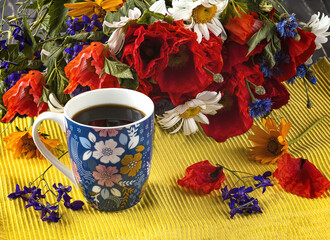 A blue cup of coffee with flowers and a bouquet of wildflowers with red poppies on a yellow background. Summer still life