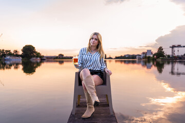 young blonde woman drinking beer sitting on the quayside of a river port