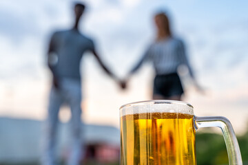 close-up of a glass of beer in front of a multiracial couple of lovers blurred in the background