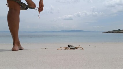Detail of woman's taking off her bikini on a nudist beach.