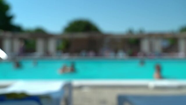 Abstract bokeh background of blurred hotel pool with blue water and swimming people. Defocused resort on hot summer day. Vacation, holiday and travel
