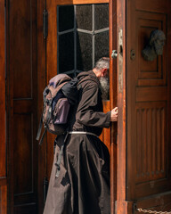Authentic Catholic pilgrim in black clothes with a large backpack behind his back, girded with a...