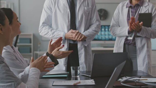 Cropped shot of professional team of doctors applauding to unrecognizable head physician during corporate meeting in office
