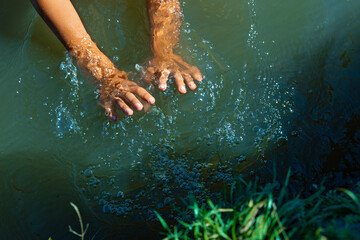 The child's hands spray dense green water in the lake. Summer activity for children - a game with clear water