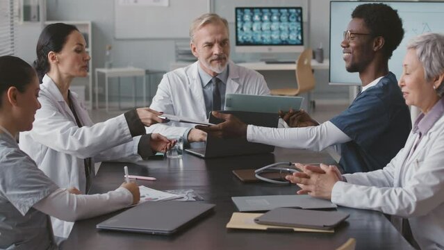 Waist up of professional multiracial medical team doing paperwork and having discussion while having corporate brief meeting with head physician at table in conference room