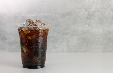 Ice americano coffee in a tall disposable glass over grey background on white table. Cold summer...