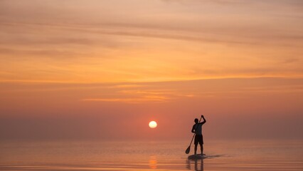 Man paddling on stand up paddle board against background of rising sun. SUP