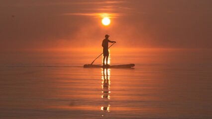 Man paddling on stand up paddle board against background of rising sun. SUP