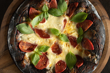Black pizza margarita with tomatoes, mozzarella and basil. Dough with healthy bamboo charcoal powder, close up