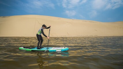 Man paddling on stand up paddle board against background of dunes in desert. SUP