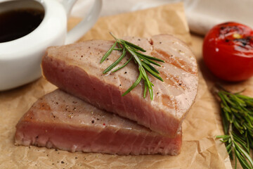 Pieces of delicious tuna with rosemary on parchment paper, closeup