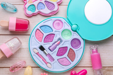 Decorative cosmetics for kids. Eye shadow palette, lipsticks and accessories on white wooden table, flat lay