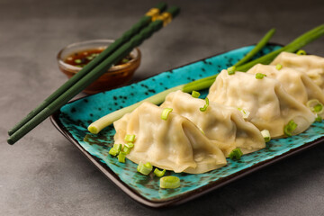 Delicious gyoza (asian dumplings) with green onions and chopsticks on gray table, closeup