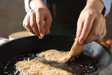 Cooking schnitzel. Woman putting raw pork chop in bread crumbs into frying pan, closeup