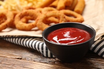 Tasty ketchup with snacks on wooden table, selective focus