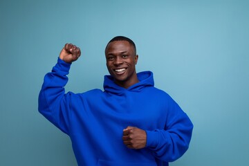 cheerful cute ethnic 25 year old african man in a stylish hoodie with a hood on a blue background