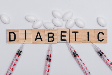 Napis diabetyk ułożony na białym tle, obok strzykawki insulinówki i lekarstwa  - obrazy, fototapety, plakaty