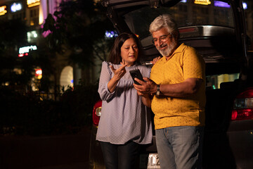 Obraz premium Happy senior citizen couple at night in market using mobile phone